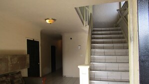 En trappa som leder upp till ett övre våningsplan, en soffa med kuddar och en lampa i taket.