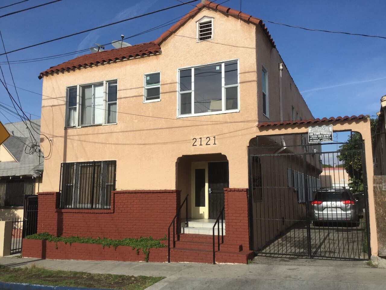 A two-story building with a beige facade and red brick base, featuring a number '2121' on the front.