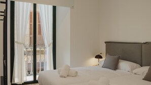 Een hotelkamer met een bed, kussens, een nachtkastje, een lamp en uitzicht door een raam met gordijnen.