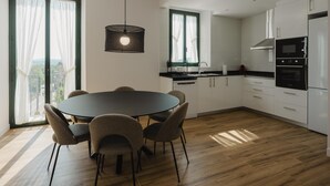 Een moderne keuken met een eethoek, met een ronde tafel met stoelen, een hanglamp en grote ramen met gordijnen.