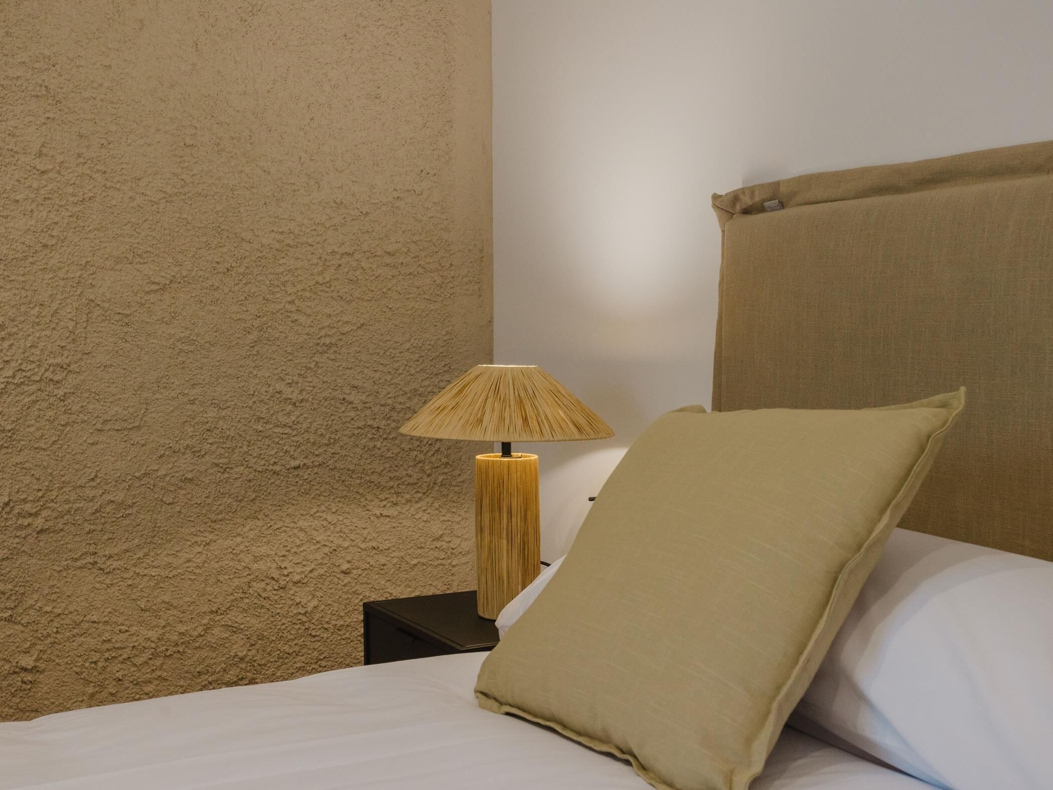 A bed with a beige pillow, a bedside lamp, and a textured wall.