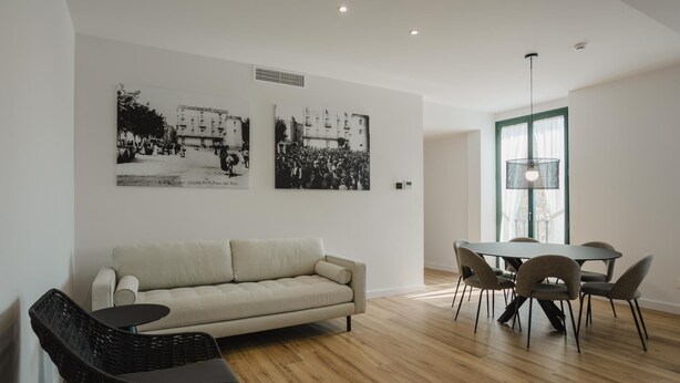 Een moderne woonkamer met een bank, een eettafel met stoelen, en twee zwart-witfoto ’s aan de muur.