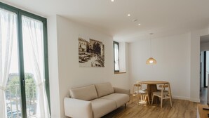 Un salon moderne avec un canapé beige, une table à manger en bois et un tableau représentant un paysage urbain accroché au mur.