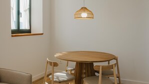 Un coin repas avec une table ronde en bois et quatre chaises, un luminaire suspendu en fibres tressées et une fenêtre avec des rideaux.