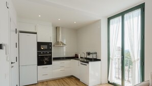 Une cuisine moderne avec des meubles blancs, un four encastré et une grande fenêtre agrémentée de rideaux.