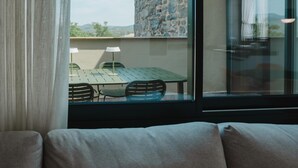 Un salon moderne donnant sur un balcon aménagé avec une table et des chaises, un mur en pierre et une porte vitrée.