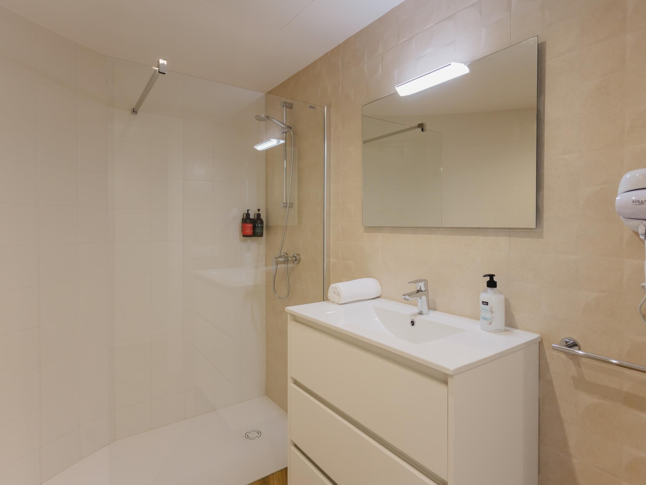 Un bany modern amb dutxa, un lavabo amb mirall i articles de tocador.