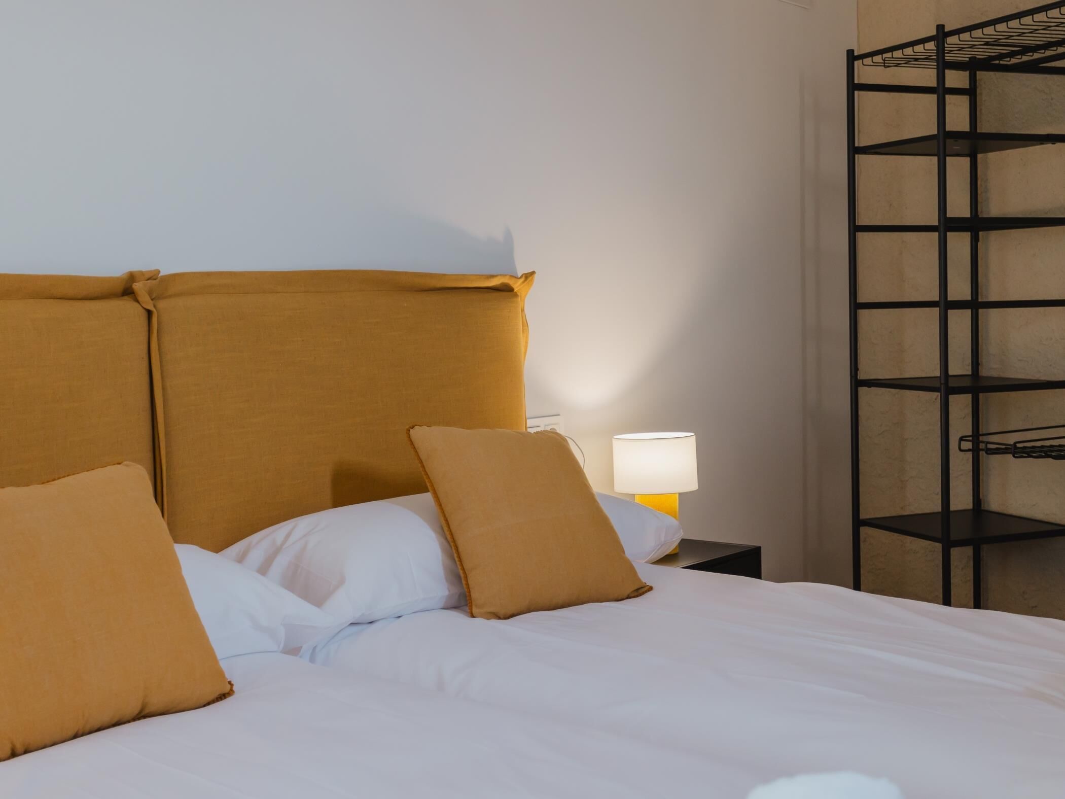 Un lit avec une tête de lit, deux oreillers, une lampe de chevet et une étagère en métal.