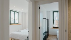A modern bedroom with a bed, a bedside table, a window with curtains, and a wooden floor.