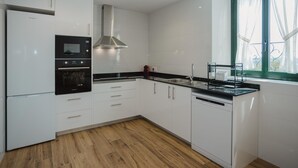 A modern kitchen with white cabinets, a built-in oven, a dishwasher, and a window with curtains.