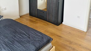 Un dormitorio con cama, piso de madera, armario y espejo.