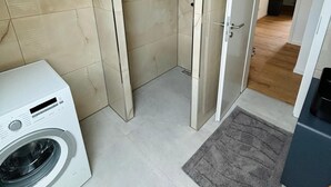 Habitación pequeña con lavadora, ducha y una puerta que da a otra habitación.