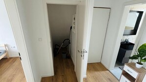 Un pasillo con suelo de madera, paredes blancas y una puerta que da a un baño.
