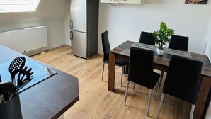 Cocina compacta con refrigerador integrado, una mesa de comedor con cuatro sillas y una pequeña planta en maceta.