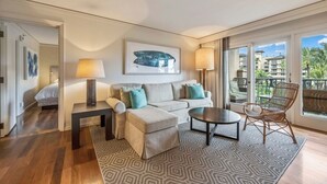 A modern living room with a sofa, ottoman, coffee table, and a chair. There are two lamps, a framed artwork on the wall, and a patterned rug. - Tropical Tranquility - Stylish Condo w/ Ocean View (Lahaina)