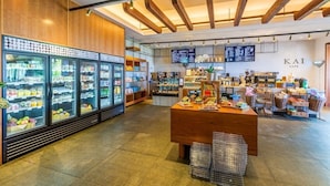 A modern cafe interior with wooden beams, a central counter, and refrigerated display cases. - Tropical Tranquility - Stylish Condo w/ Ocean View (Lahaina)