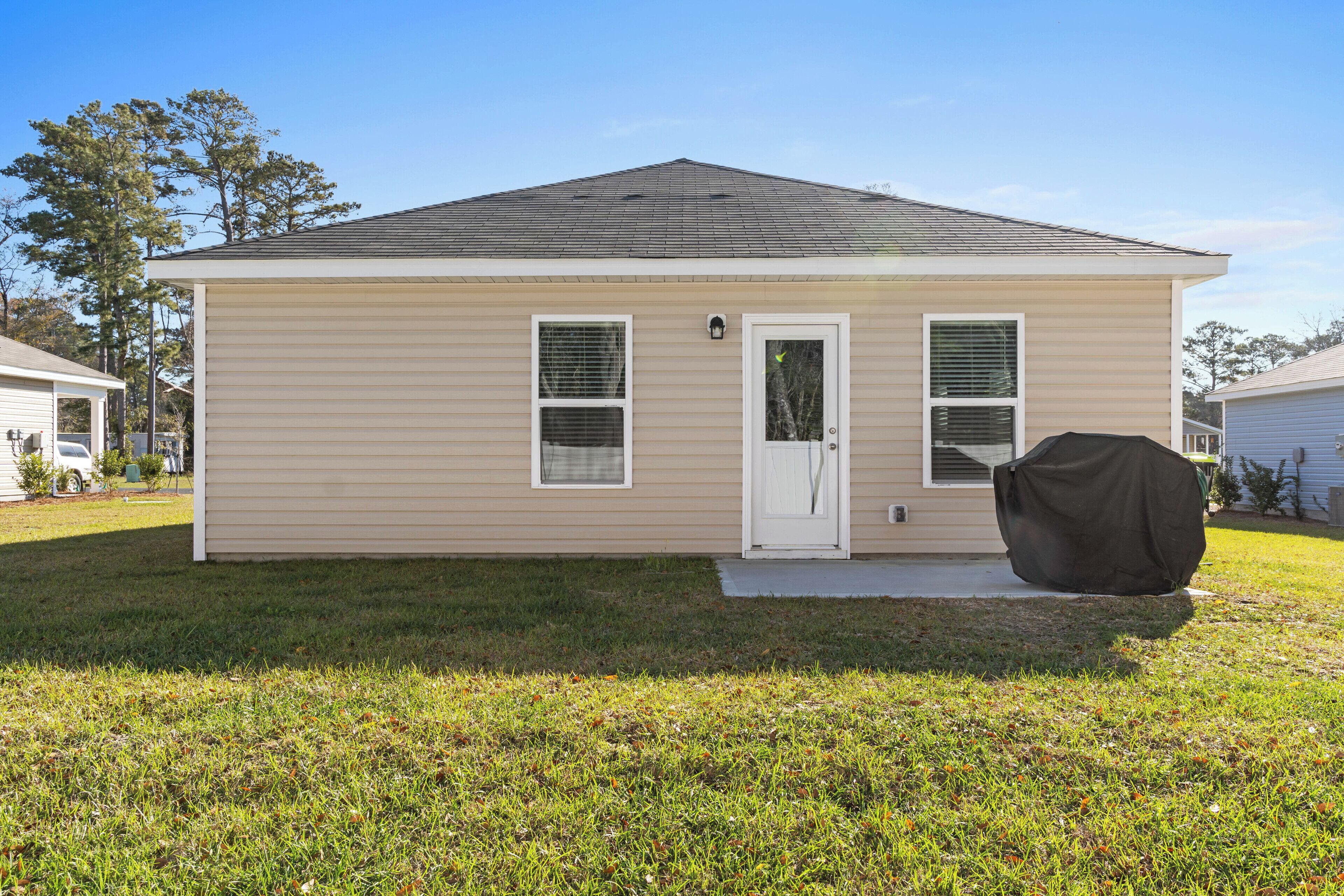 A single-story house with a beige exterior, a front door, two windows, and a covered grill.