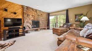 Ein Wohnzimmer mit einer Steinwand, einem Kamin, Ledersofas, einem Fernseher und einem großen Fenster.
