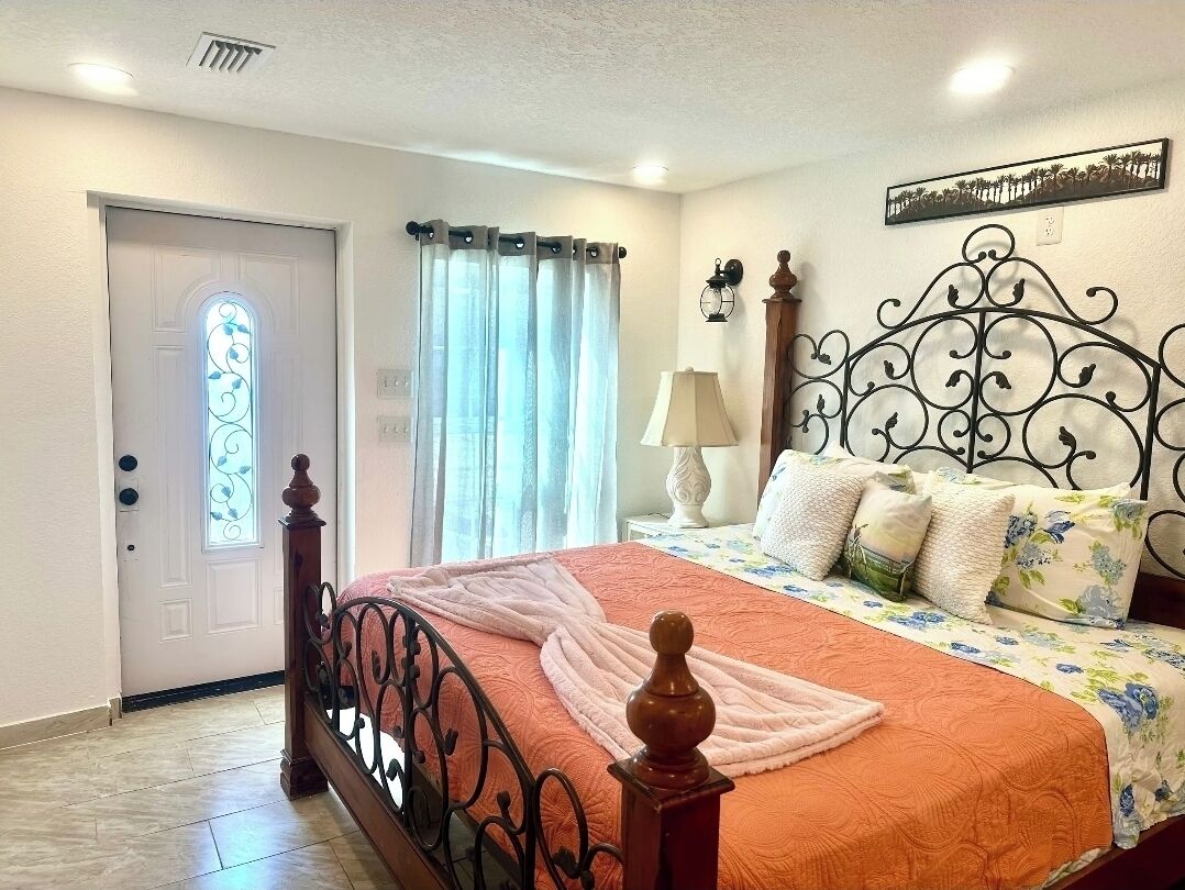A bedroom with a bed, curtains, a lamp, and a decorative wall piece.