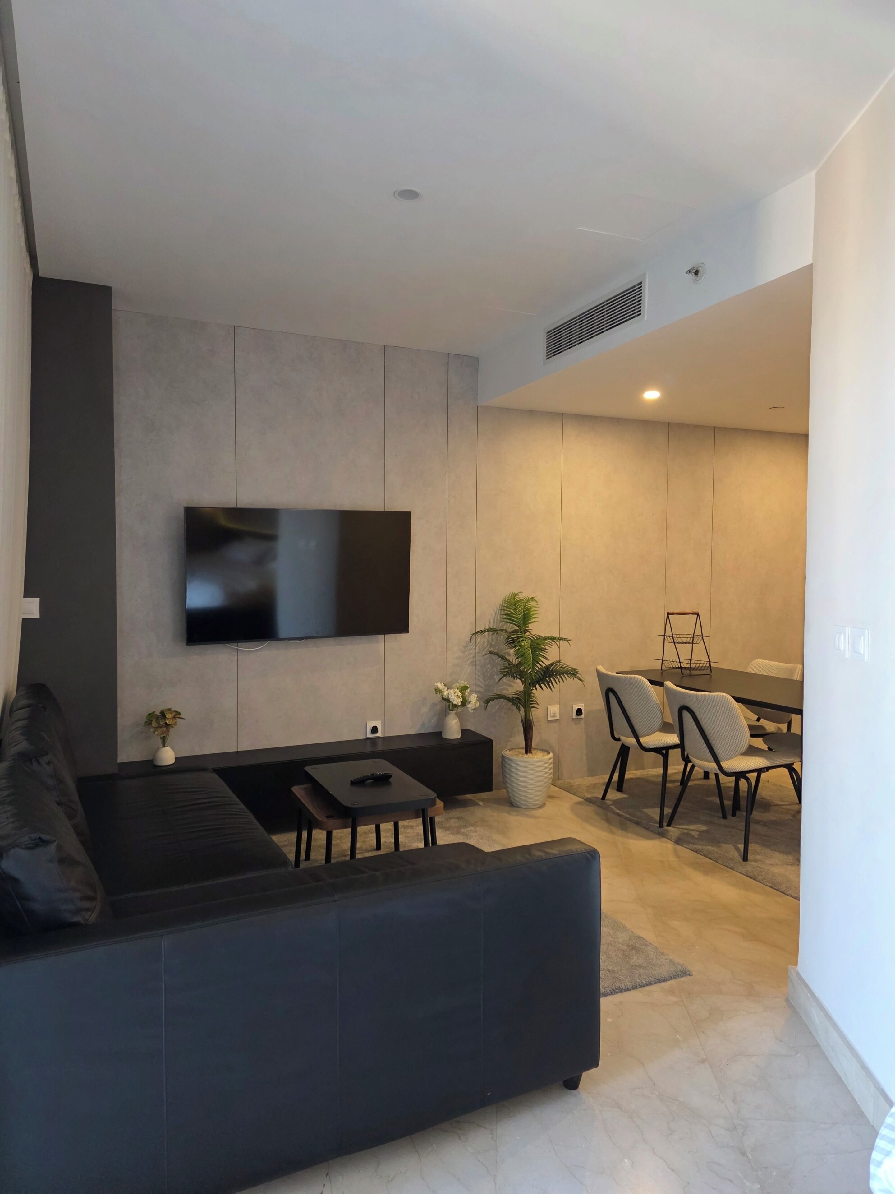 Un soggiorno moderno con una TV a schermo piatto, un divano scuro, un tavolino da caffè e una zona pranzo con sedie e tavolo.