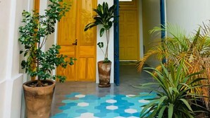 Un couloir avec une porte en bois, des plantes en pot et un sol à motifs bleus.