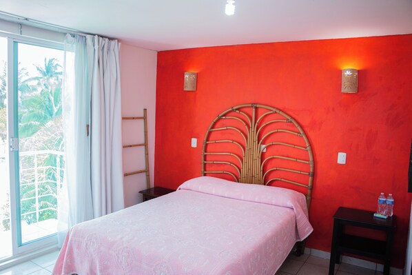 Une chambre à coucher avec un lit, une table de chevet, une fenêtre avec des rideaux et un mur rouge.