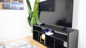 Un salon moderne avec un téléviseur à écran plat fixé sur un meuble noir, une table basse en verre sur laquelle est posée une carte, et une grande plante verte.