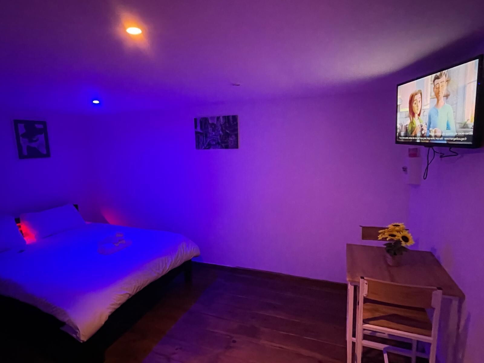 A room with a bed, a desk, and a TV on the wall.