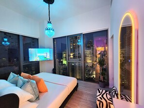 Ein modernes Schlafzimmer mit Blick auf die Stadt, einem großen Bett, einem Fernseher und einer außergewöhnlichen Deckenleuchte.