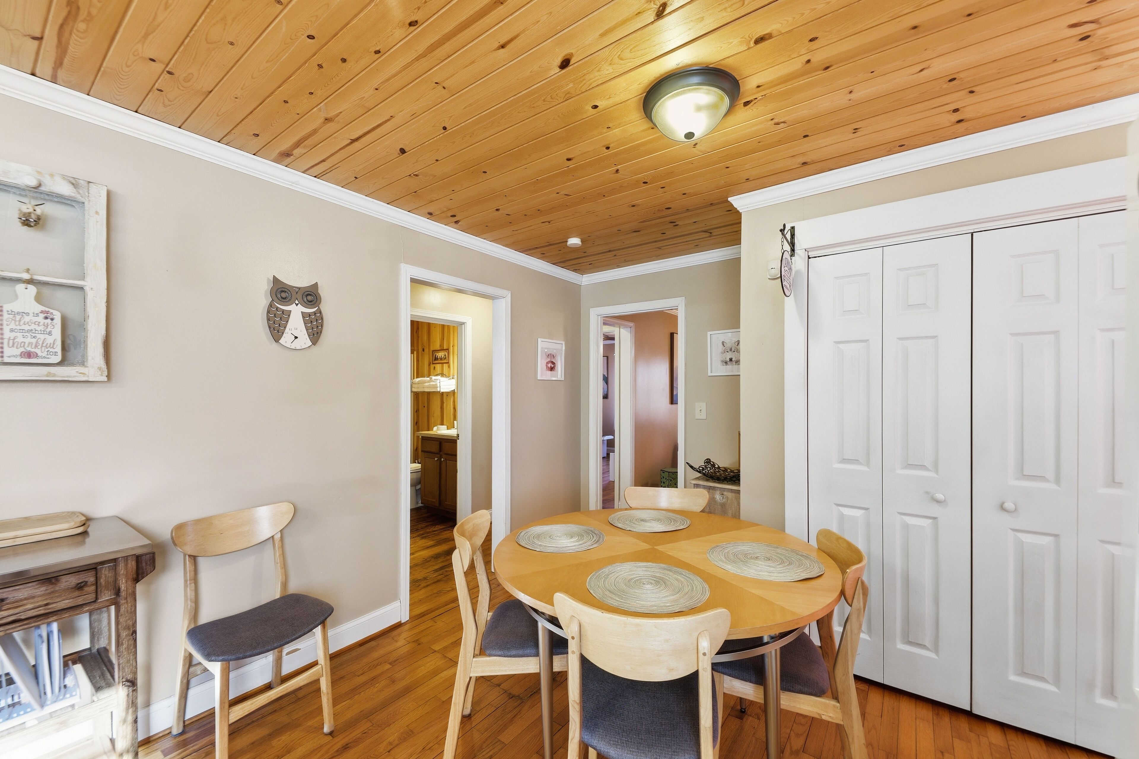 A dining area with a wooden table and chairs, a white door, and a ceiling with wooden beams.