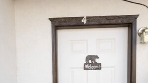 Une porte blanche avec une pancarte « Bienvenue » et la silhouette d’un ours, le chiffre « 4 » au-dessus, et un bouton d’appel à droite.