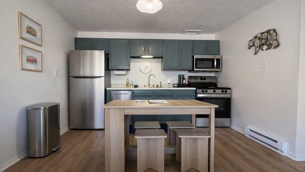 Une cuisine moderne avec des armoires de couleur turquoise, des appareils en acier inoxydable et une table en bois.