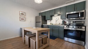Une cuisine moderne avec un plancher en bois, des armoires vertes, des appareils électroménagers en acier inoxydable et une table à manger en bois avec des bancs.