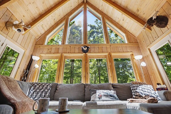 A wooden cabin with a high ceiling, large windows, a sofa with patterned cushions, and a mounted animal head. - Harbor Springs Lodge, Less then a mile to Nubs/Highlands
Ski,Golf, Hot Tub, (Harbor Springs)