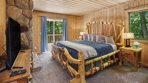 A wooden cabin bedroom with a stone wall, a bed with a wooden headboard, a television, and a window with a view of trees. - Harbor Springs Lodge, Less then a mile to Nubs/Highlands
Ski,Golf, Hot Tub, (Harbor Springs)