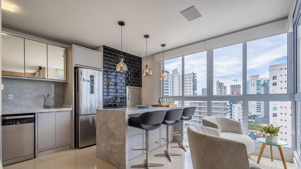 Une cuisine moderne dotée d’un îlot central, de tabourets de bar et d’une grande fenêtre donnant sur la ville.