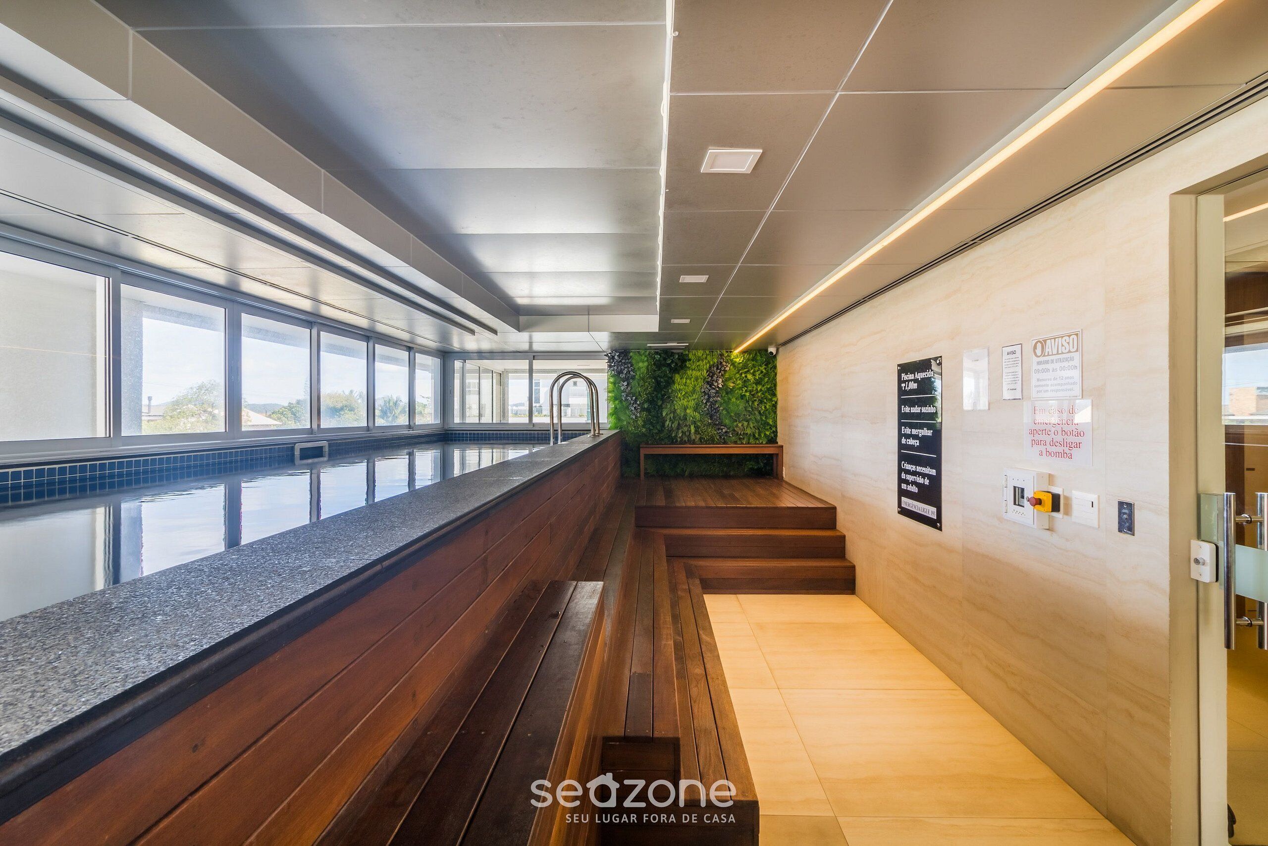 A corridor with wooden benches, a green wall, and a tiled floor.