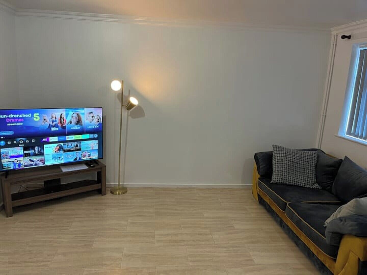 A living room with a flat-screen TV displaying a streaming service interface, a floor lamp, and a sofa with cushions.