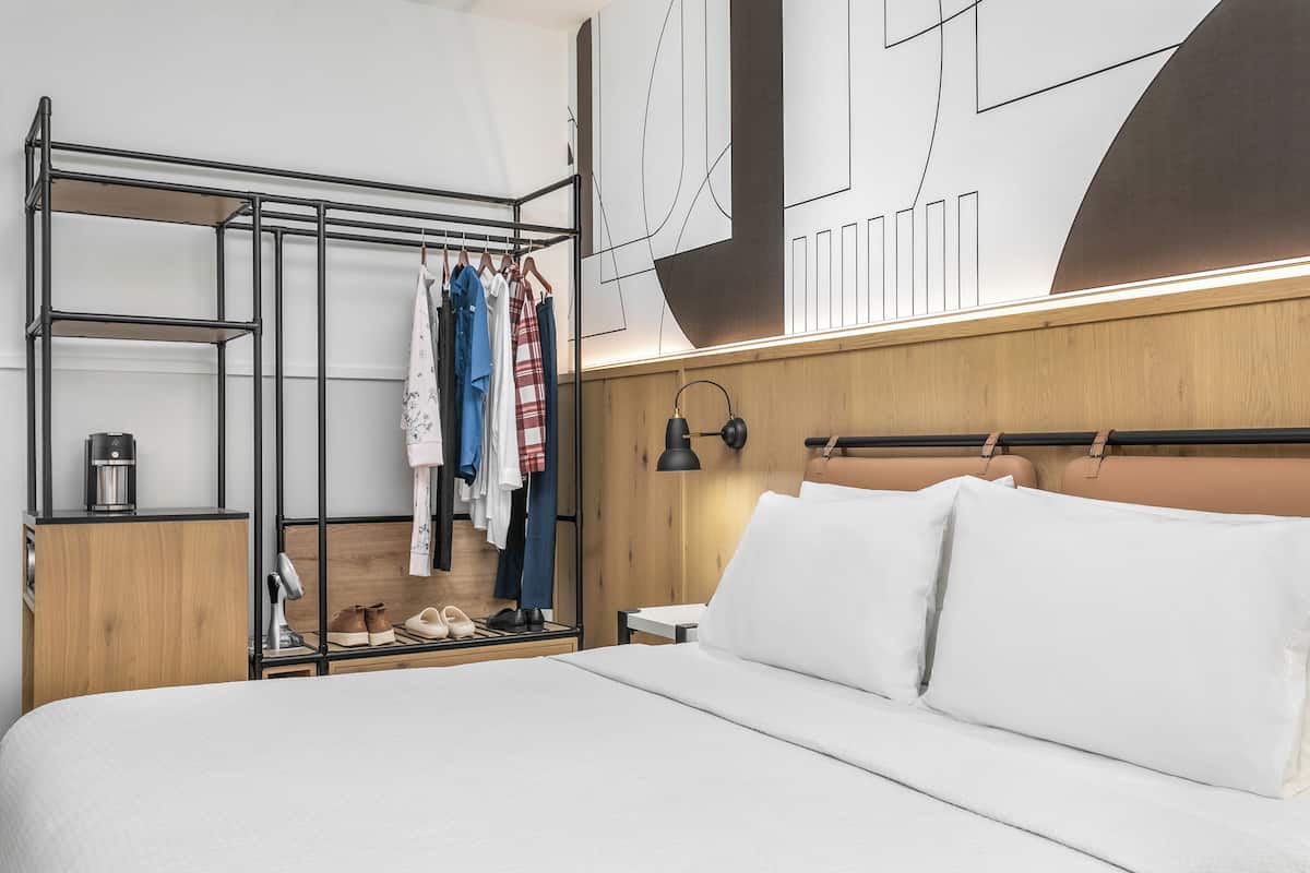 A modern hotel room with a bed, a wardrobe, and a mirror.