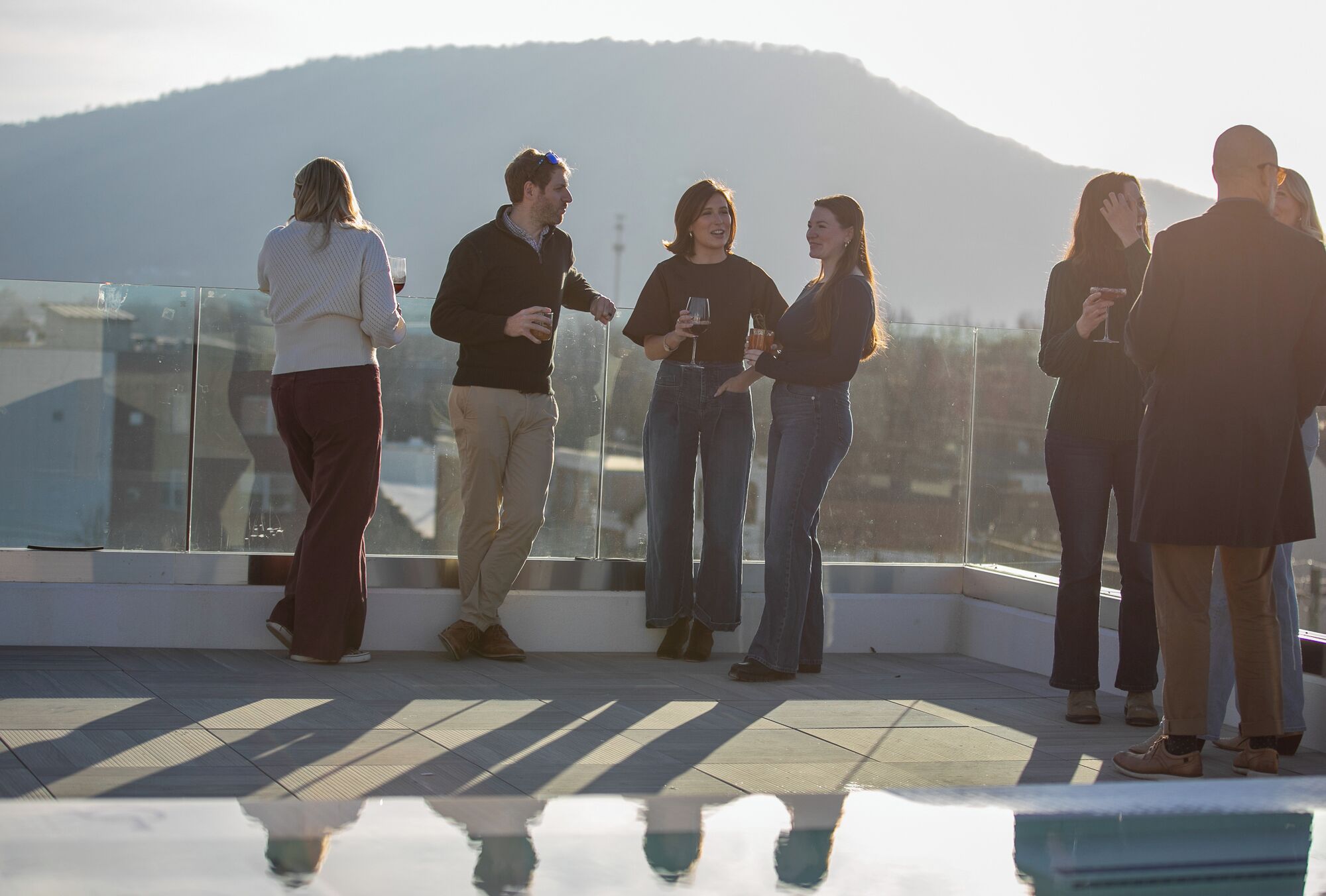 A group of people standing on a rooftop terrace with a mountain in the background.