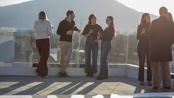 A group of people standing on a rooftop terrace with a mountain in the background.