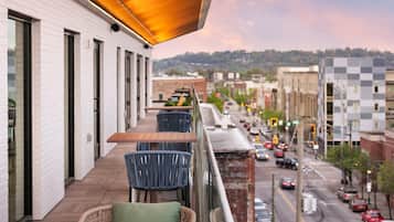 A balcony with outdoor seating, overlooking a city street with buildings and cars.