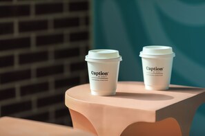 Deux tasses à café de la marque Caption by Hyatt sont posées sur une table, devant un mur de briques et sur un fond turquoise.