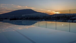 A glass-enclosed infinity pool with a view of a mountain and a sunset.