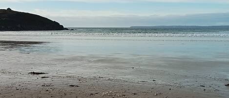 Une plage de galets et de rochers, avec une eau calme et une côte rocheuse qui s’étend au loin.