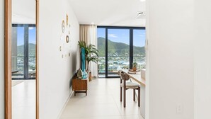 A modern room with a large window, a dining area, and a view of a cityscape and hills. - D434 - Amazing Apartment with Balcony (Sint Maarten)