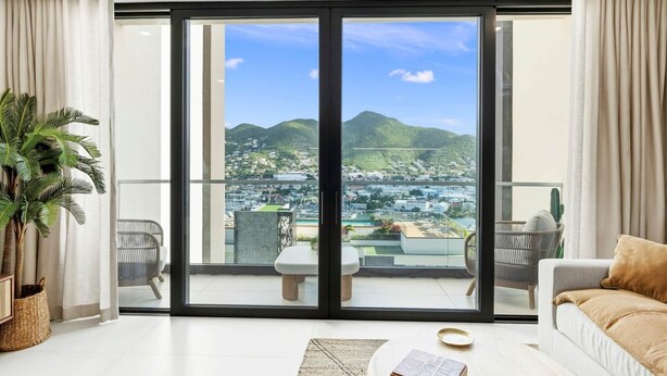 A modern living room with a large sliding glass door leading to a balcony with a city view. - D434 - Amazing Apartment with Balcony (Sint Maarten)