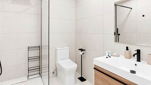A modern bathroom with a glass-enclosed shower, a toilet, a sink with toiletries, and a mirror. - D434 - Amazing Apartment with Balcony (Sint Maarten)
