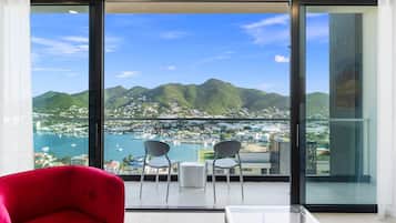Una habitación moderna con puerta de vidrio que da a un balcón con vistas a un puerto deportivo y montañas.