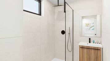 Un baño moderno con ducha de vidrio, un lavabo blanco con mueble de madera y un espejo grande.